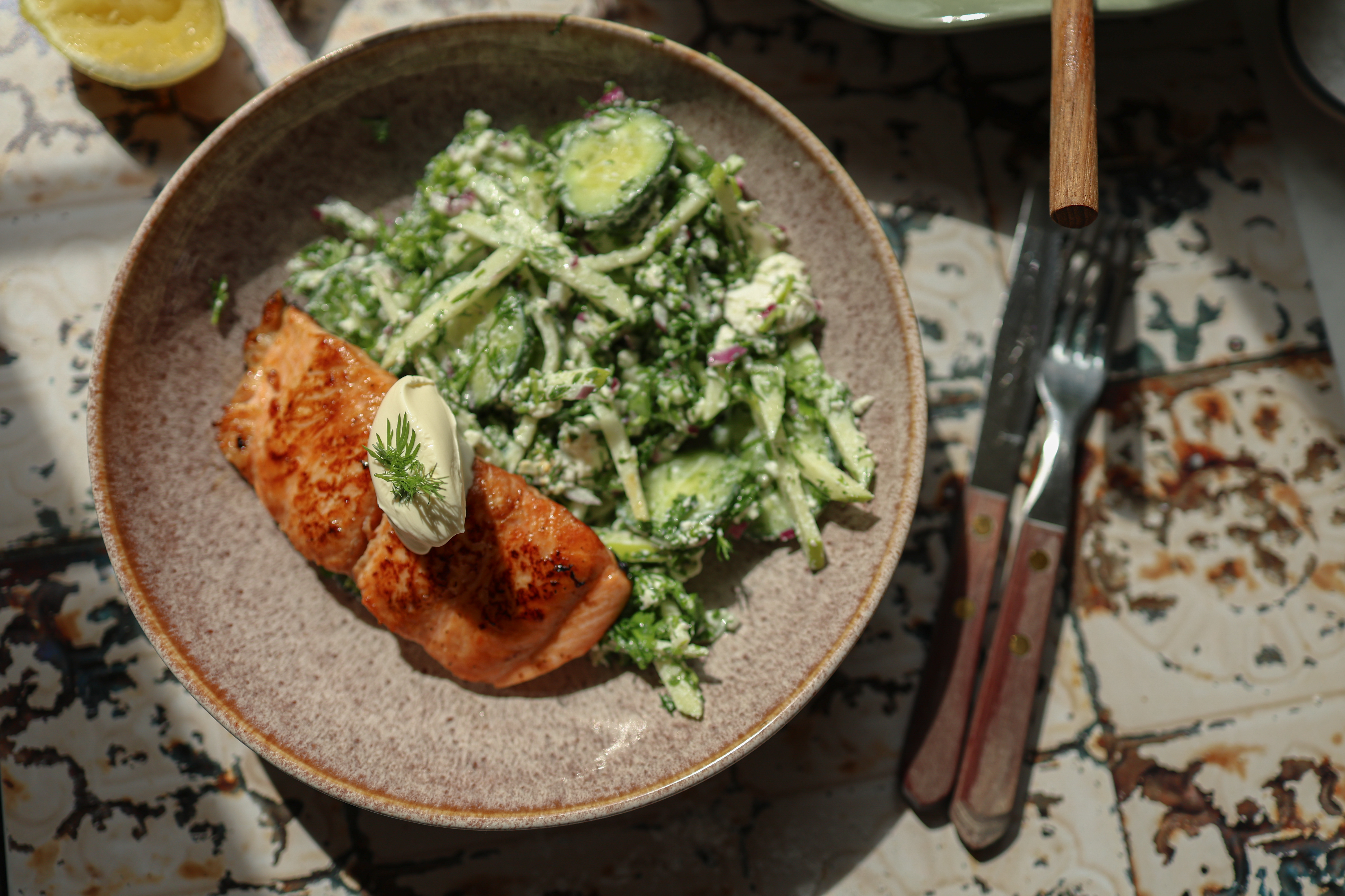 En tallerken med stekt laks, grønnfarget salat og en klatt rømme oppå. 