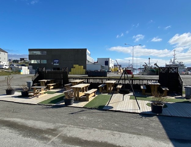 Park area with benches, a bonfire and green areas, in the back is a square factory with the Lerøy-logo.