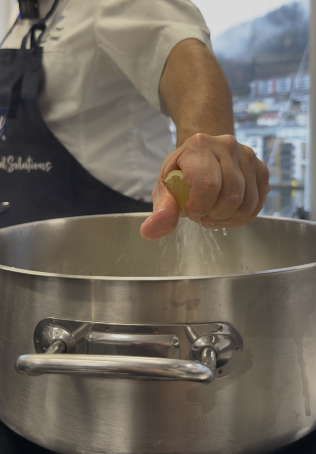 En hånd som skviser en sitronbit over en panne. 