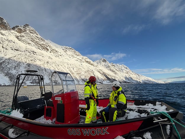 En kvinne og mann ikledd arbeidsklær snakker på en båt. 