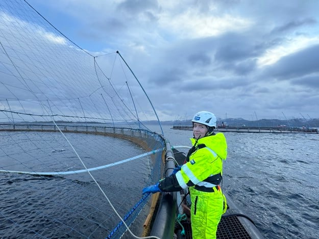 Ung kvinne med arbeidsklær ute på merdkanten. 