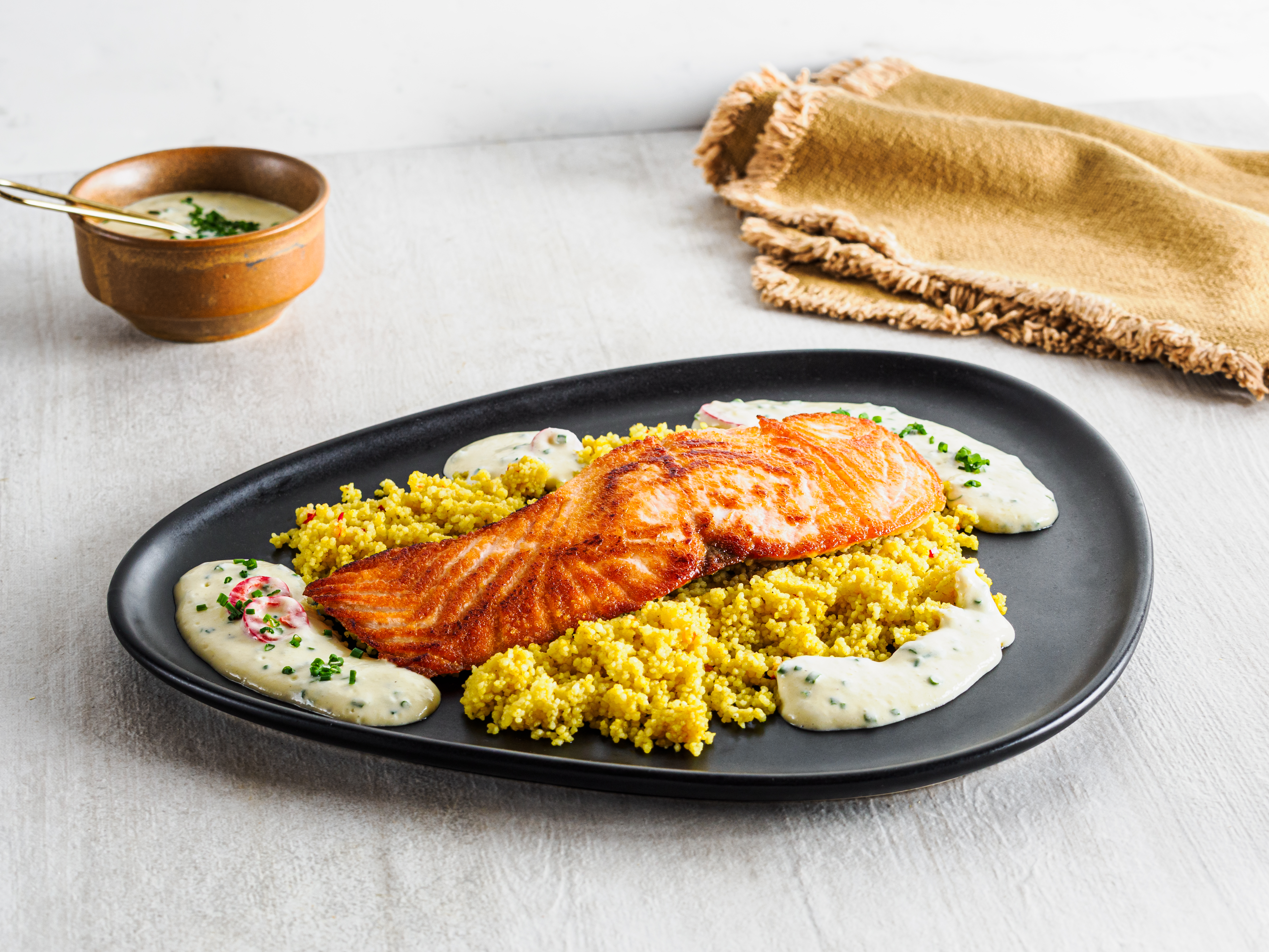 Mørkt fat med laks lagt på gul couscous med saus rundt. 
