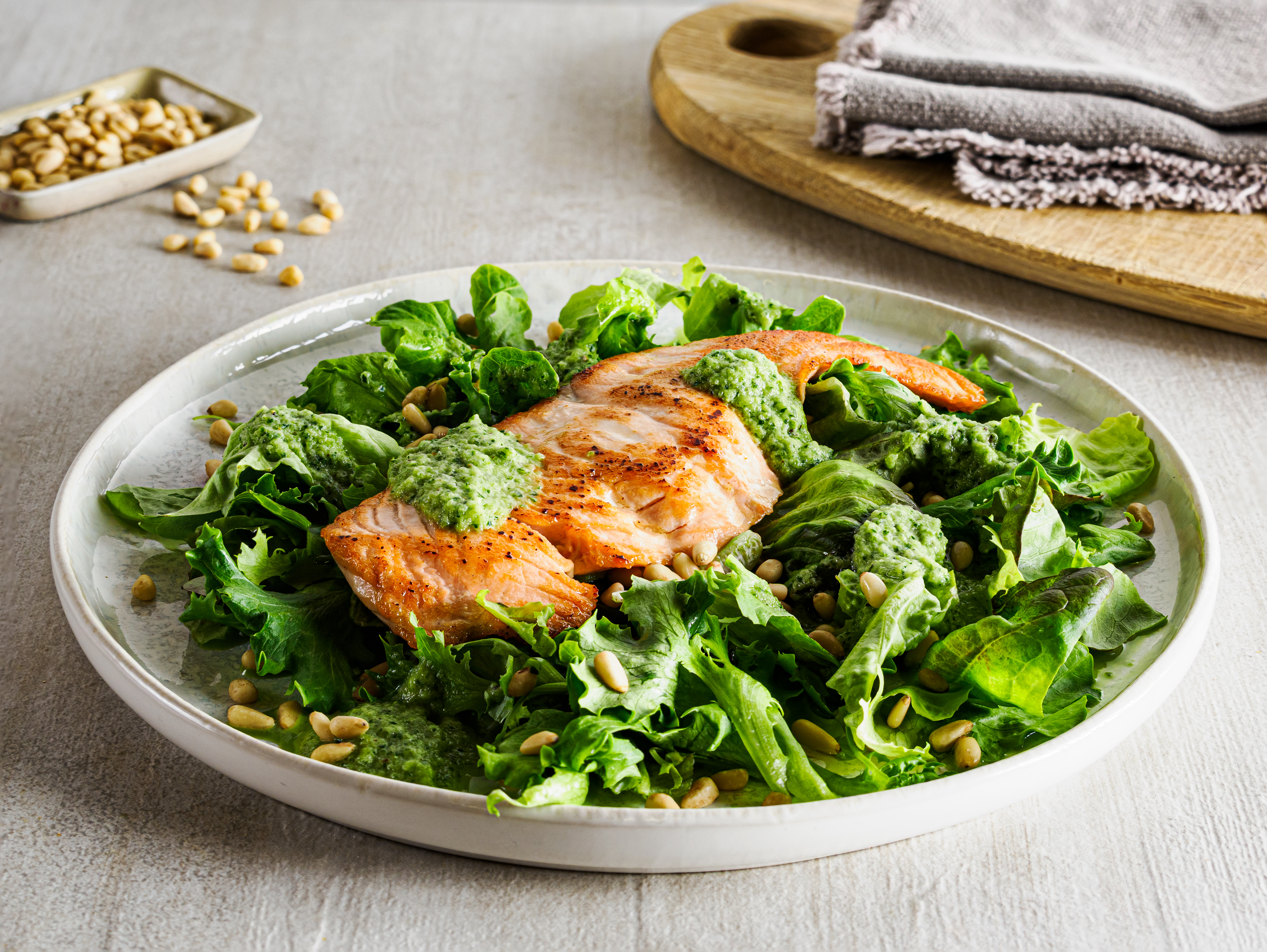 Stekt laks med agurkvinaigrette, salat og pinjekjerner servert på hvitt fat