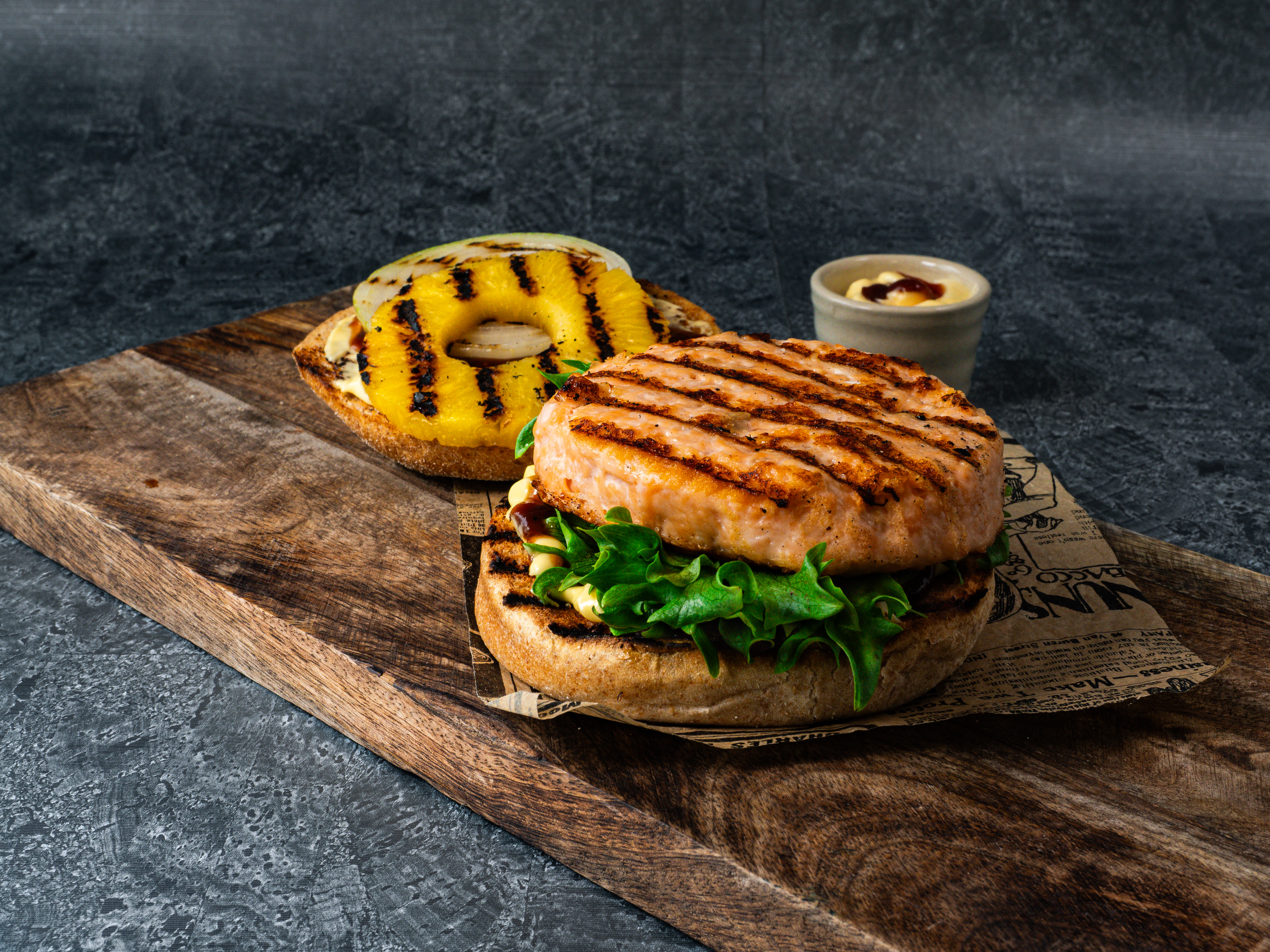 Fiskeburger av laks med BBQ-saus og grillet løk og ananas på et skjærebrett