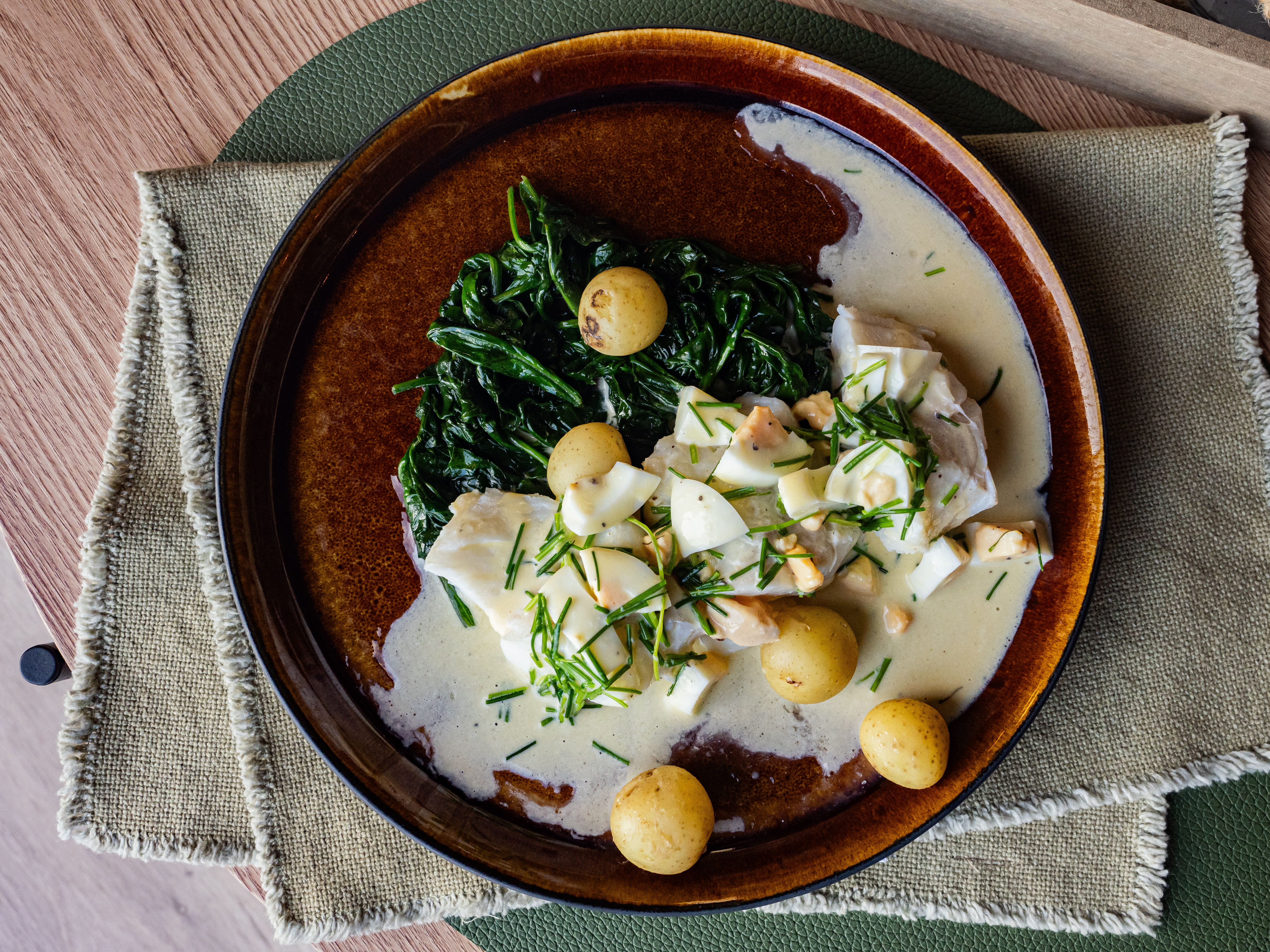 En tallerken på et bord med skrei med eggesmør, spinat og småpoteter