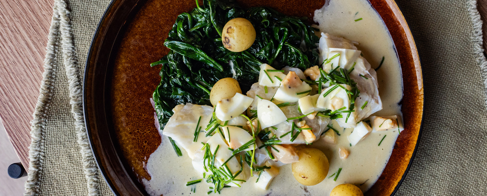 En tallerken på et bord med skrei med eggesmør, spinat og småpoteter