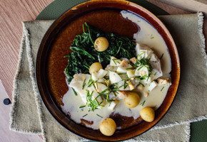 En tallerken på et bord med skrei med eggesmør, spinat og småpoteter